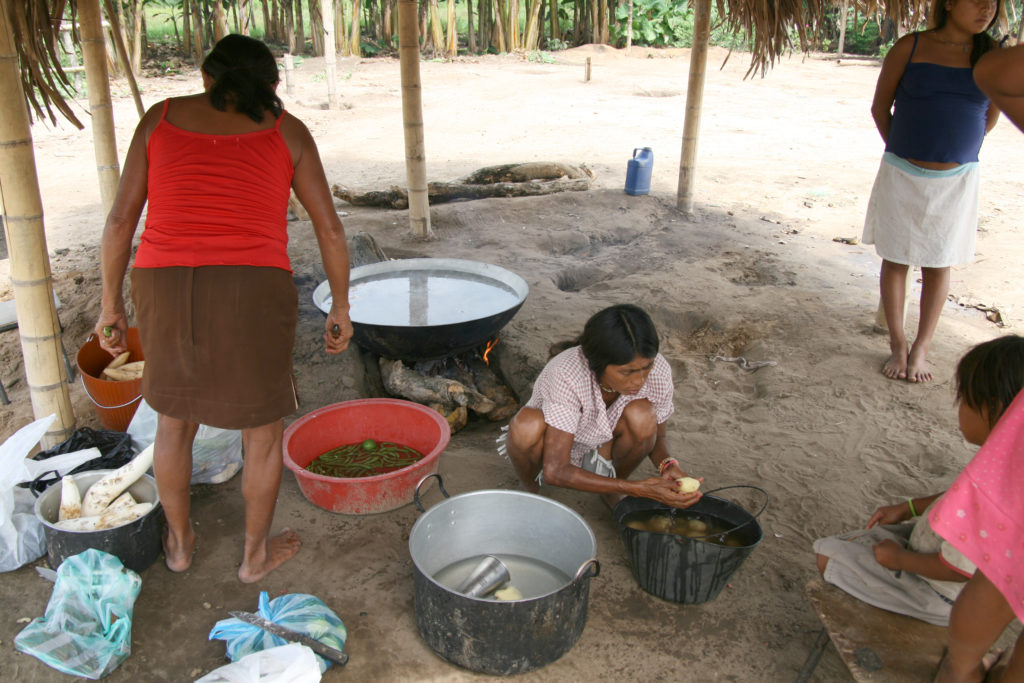 Bild på två människor ur lokalbefolkningen som tillagar mat i kastruller på marken.